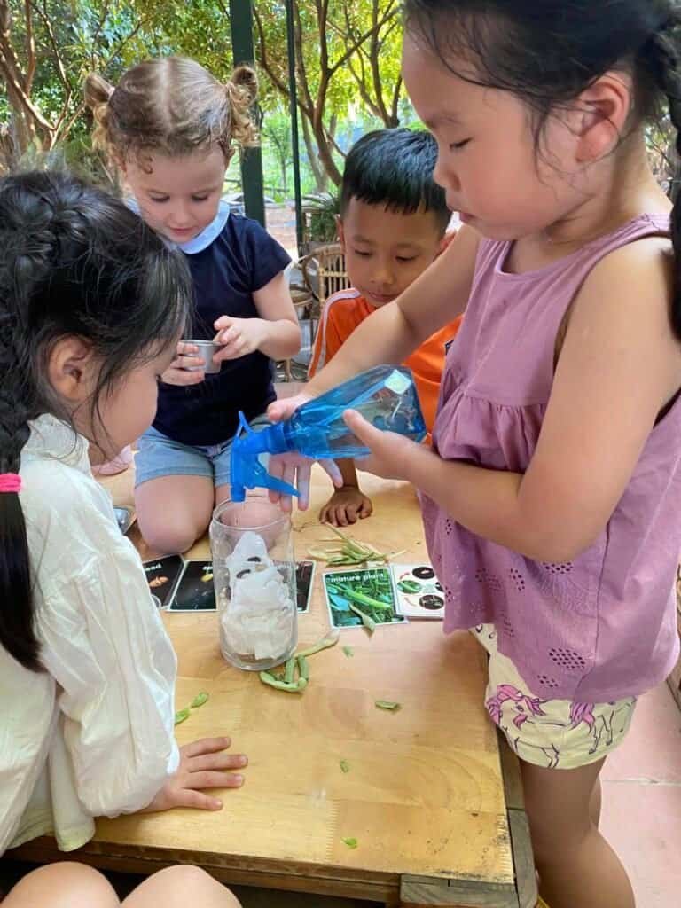 Children engaging in outdoor science activity with a blue watering can.