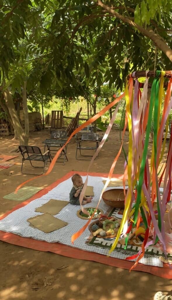 Children's outdoor play area with colorful ribbons and mats under trees.
